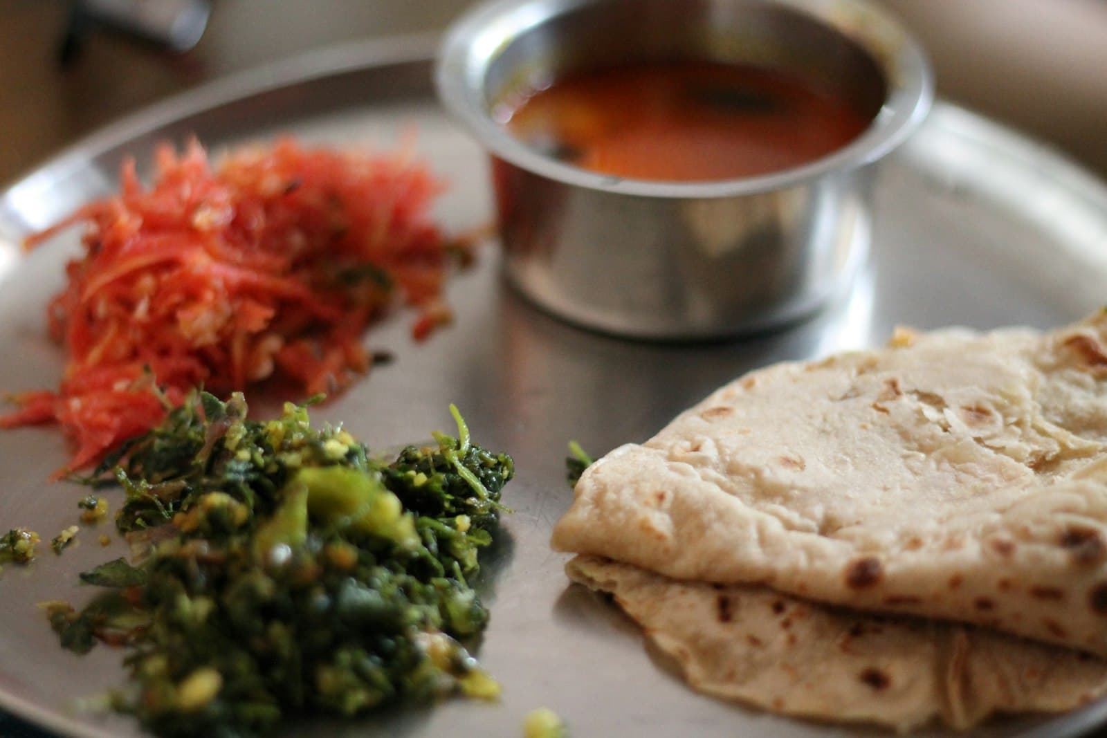 Soft chapatis with leafy green sabzi and grated carrot on a steel plate